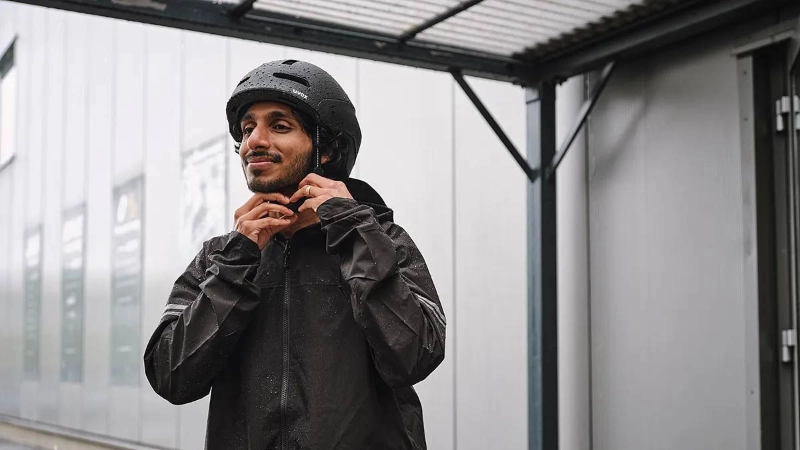 Ein Mann mit Regenmantel zieht sich einen schwarzen Helm auf und steigt auf sein Fahrrad