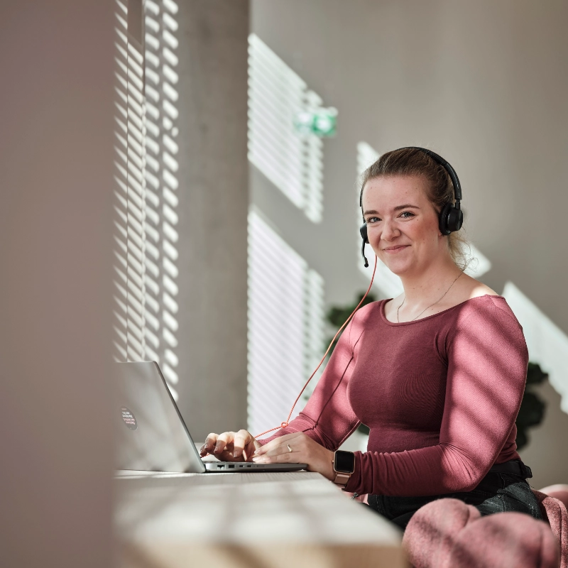 JobRad-Mitarbeiterin mit rotem shirt sitzt am Laptop und lächelt dich an